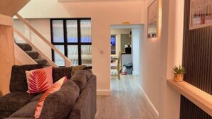 A modern living room with a grey sofa, wooden flooring, a staircase, and a hallway leading to another room. - Stylish City Centre Hideaway & Hot Tub (Galway)