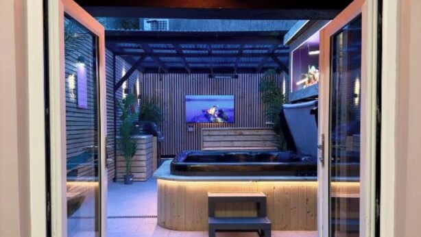 A modern outdoor patio with a hot tub, a television screen, and a wooden deck. - Stylish City Centre Hideaway & Hot Tub (Galway)