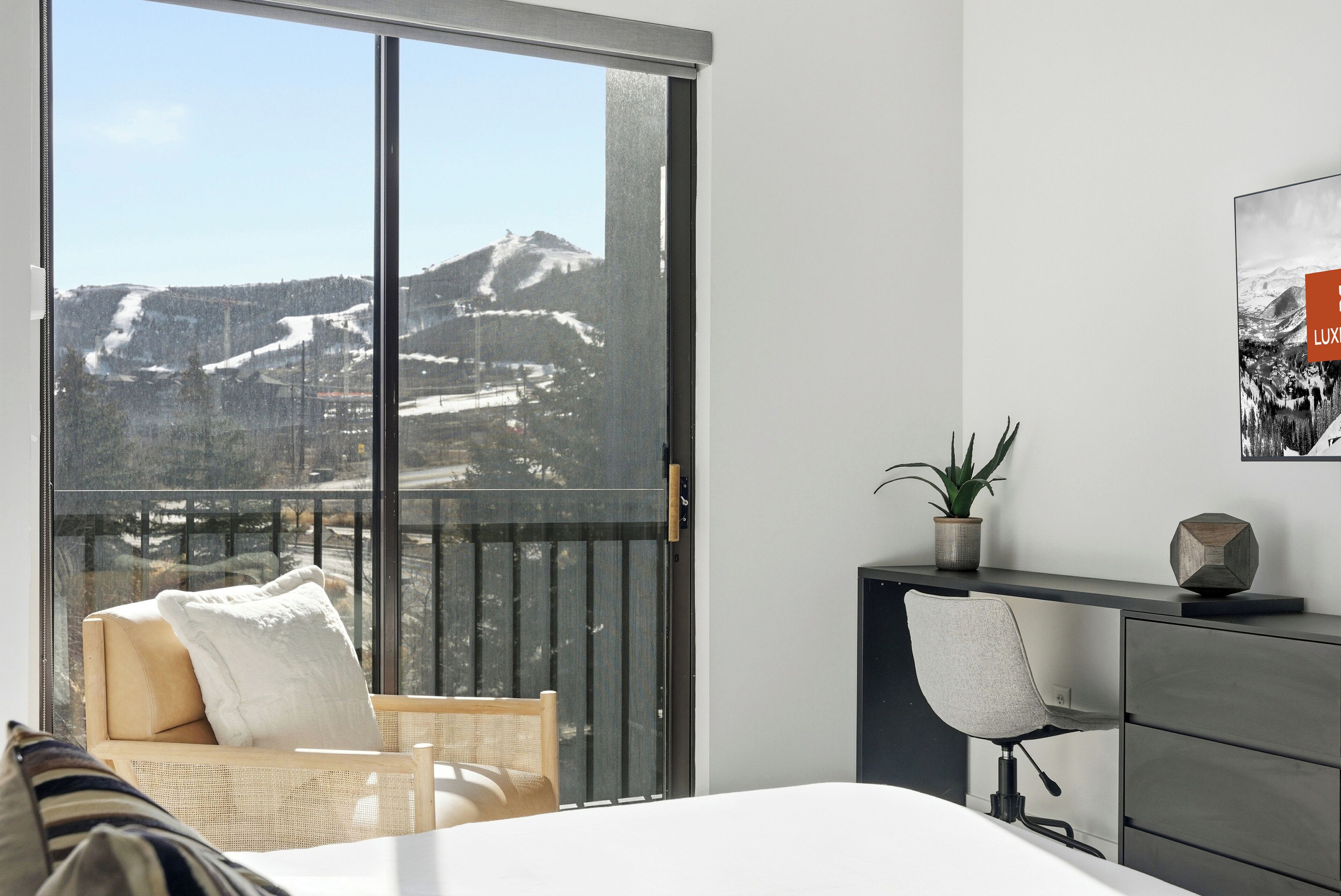 A modern hotel room with a large sliding glass door leading to a balcony with a mountain view.