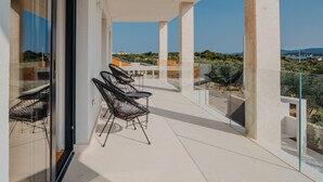 Un balcón moderno con barandillas de vidrio, un espacio de descanso con sillas y una vista despejada del paisaje circundante.