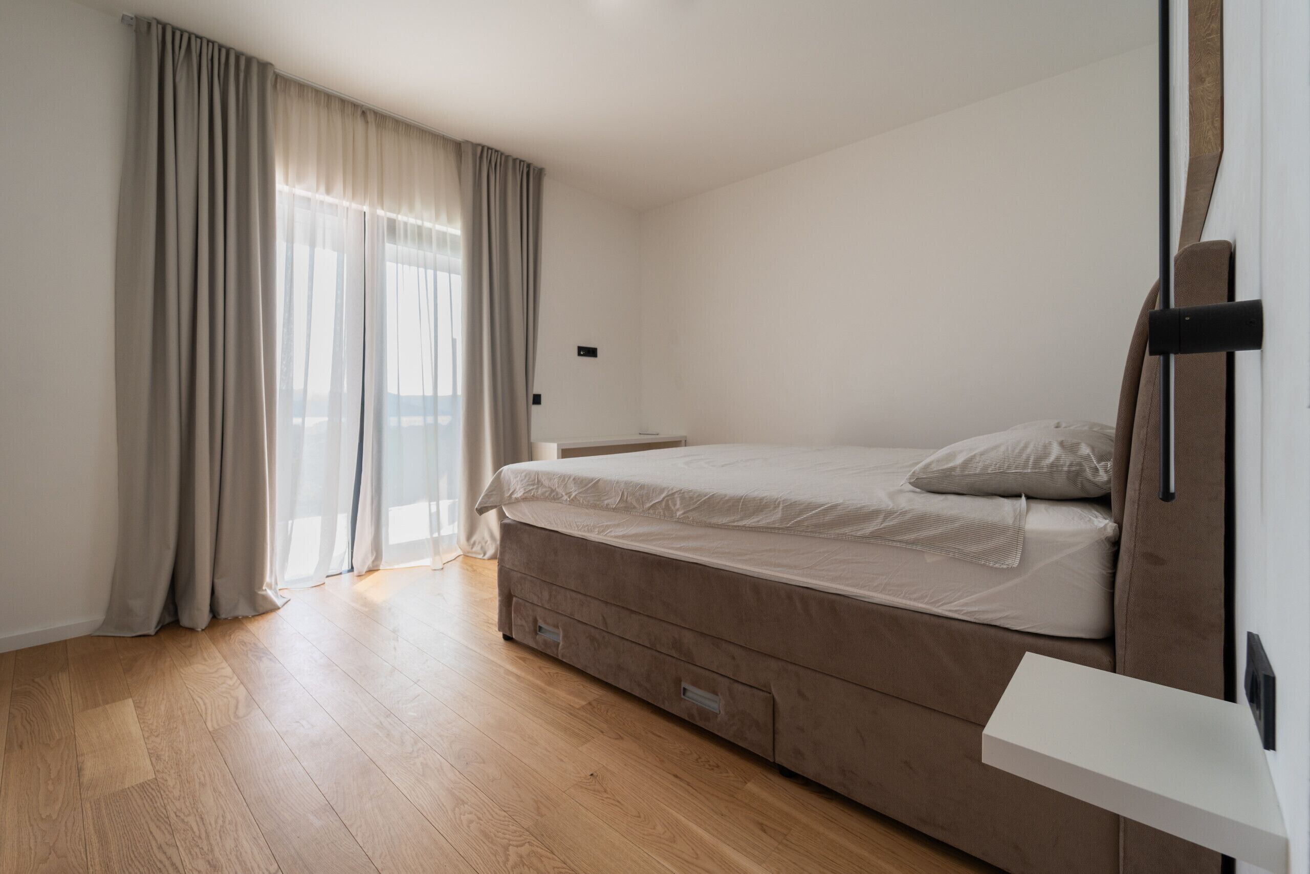 A bedroom with a bed, a bedside table, a wardrobe, and a window with curtains.