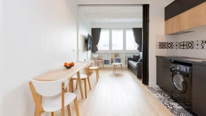 A modern kitchen with a built-in washing machine, a dining area with a table and chairs, and a view into the living room. - Modern apartment with plenty of public transport! (Neuilly-sur-Seine)