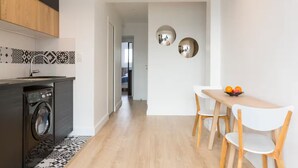 A modern kitchen with a washing machine, a dining area with a table and chairs, and a hallway leading to another room. - Modern apartment with plenty of public transport! (Neuilly-sur-Seine)