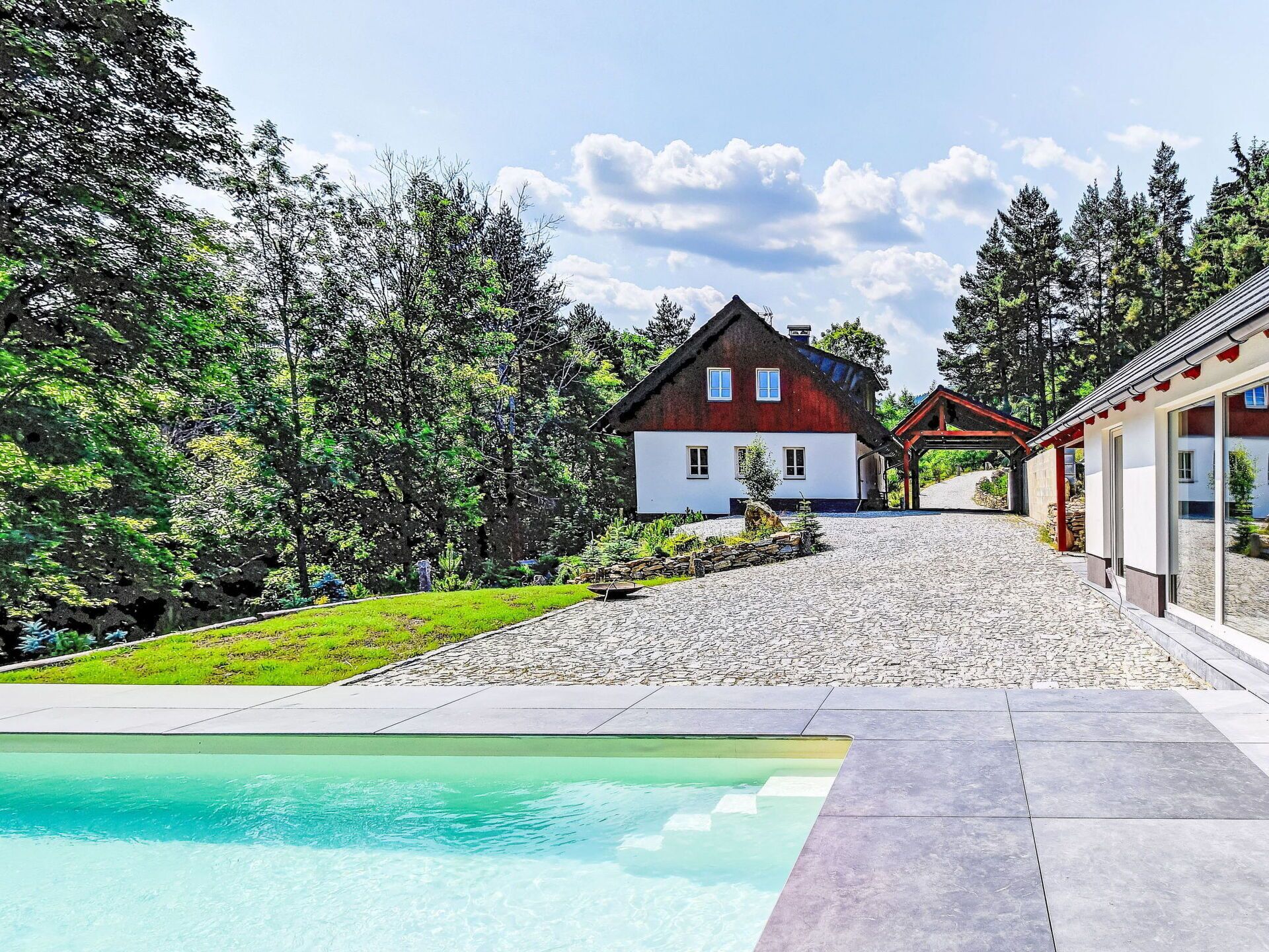 Una casa circondata da alberi, con piscina e un vialetto in pietra.