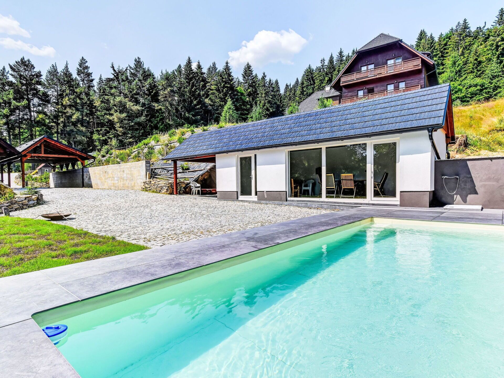 A modern house with a swimming pool, large windows, and a stone patio.