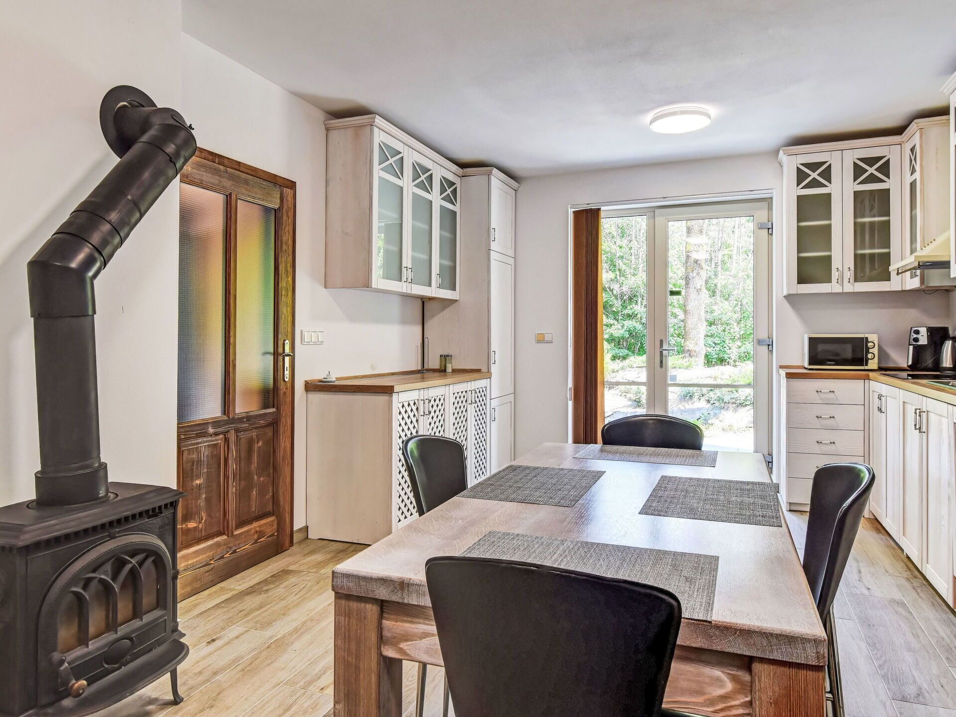 A compact kitchen with a wood-burning stove, white cabinets, and a dining area with a table and chairs.