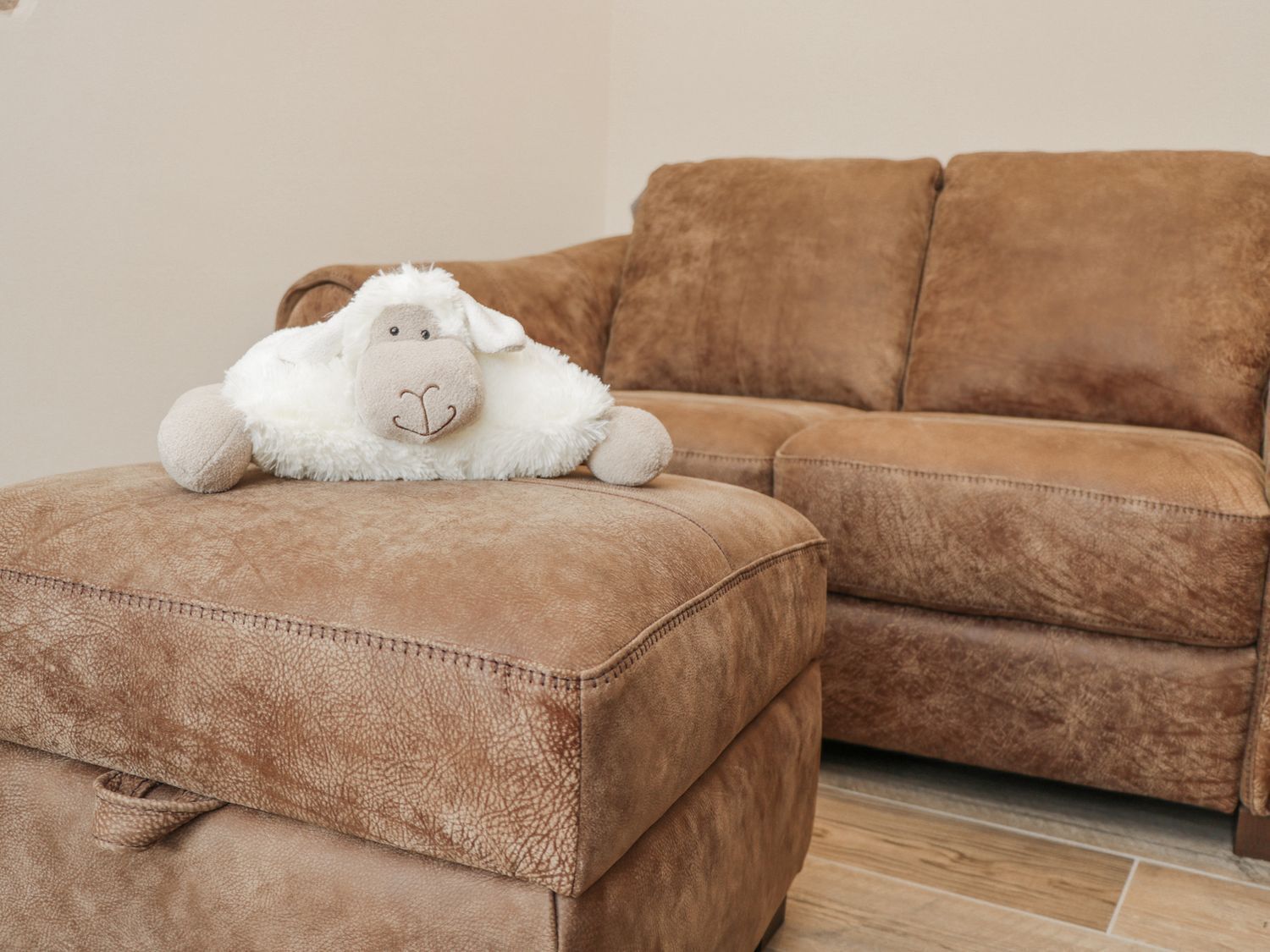 A brown leather sofa with a plush white sheep toy on a matching ottoman.