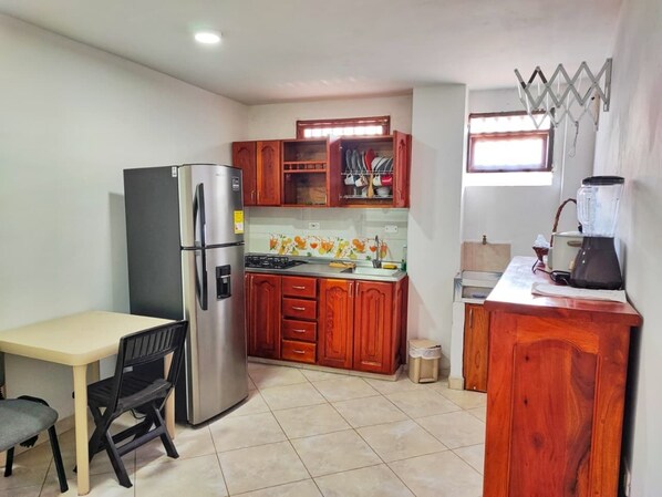 A compact kitchen with a refrigerator, wooden cabinets, a sink, and a dining area with a table and chairs.