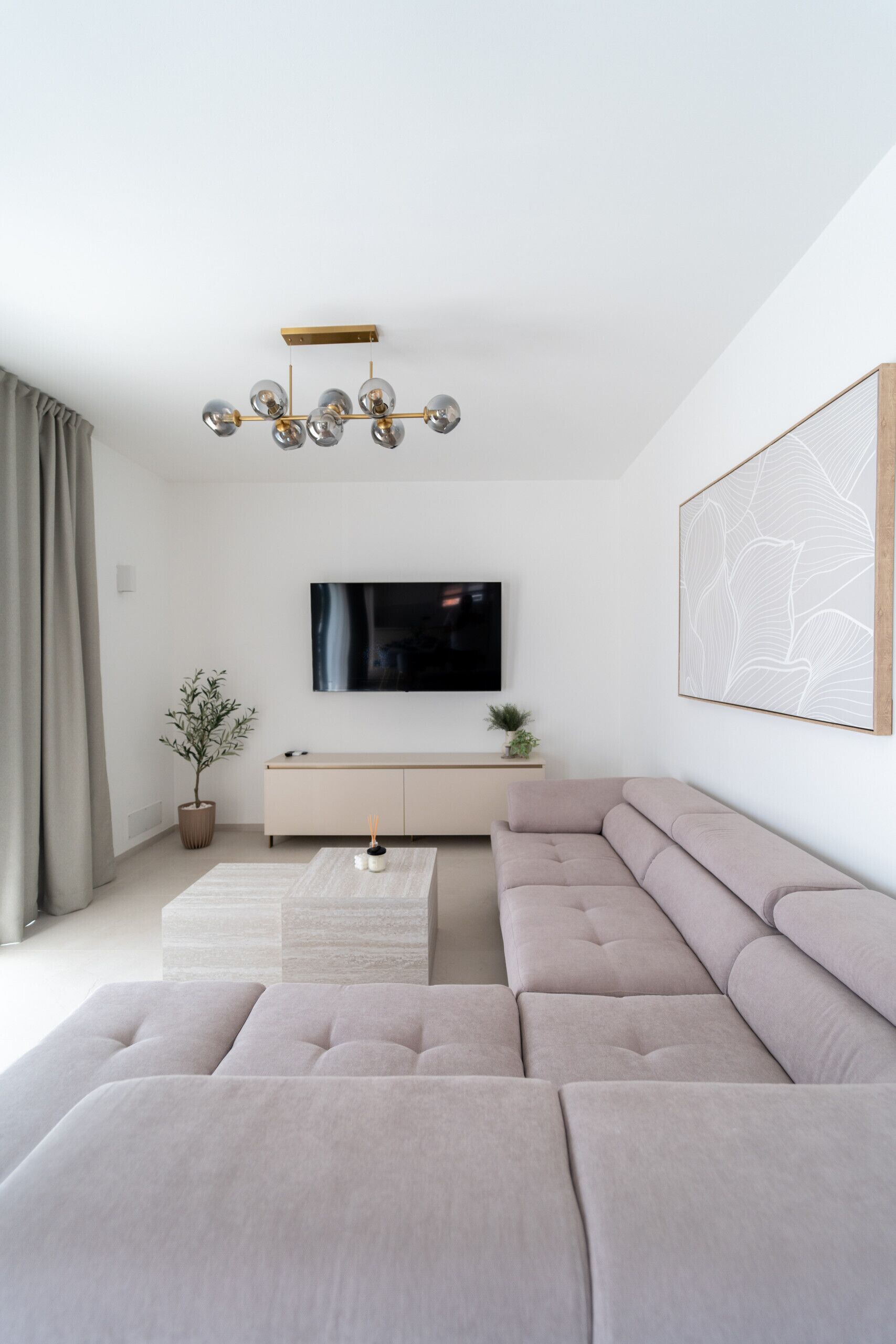 A modern living room with a sectional sofa, a flat-screen TV, a minimalist console table, and a decorative light fixture.