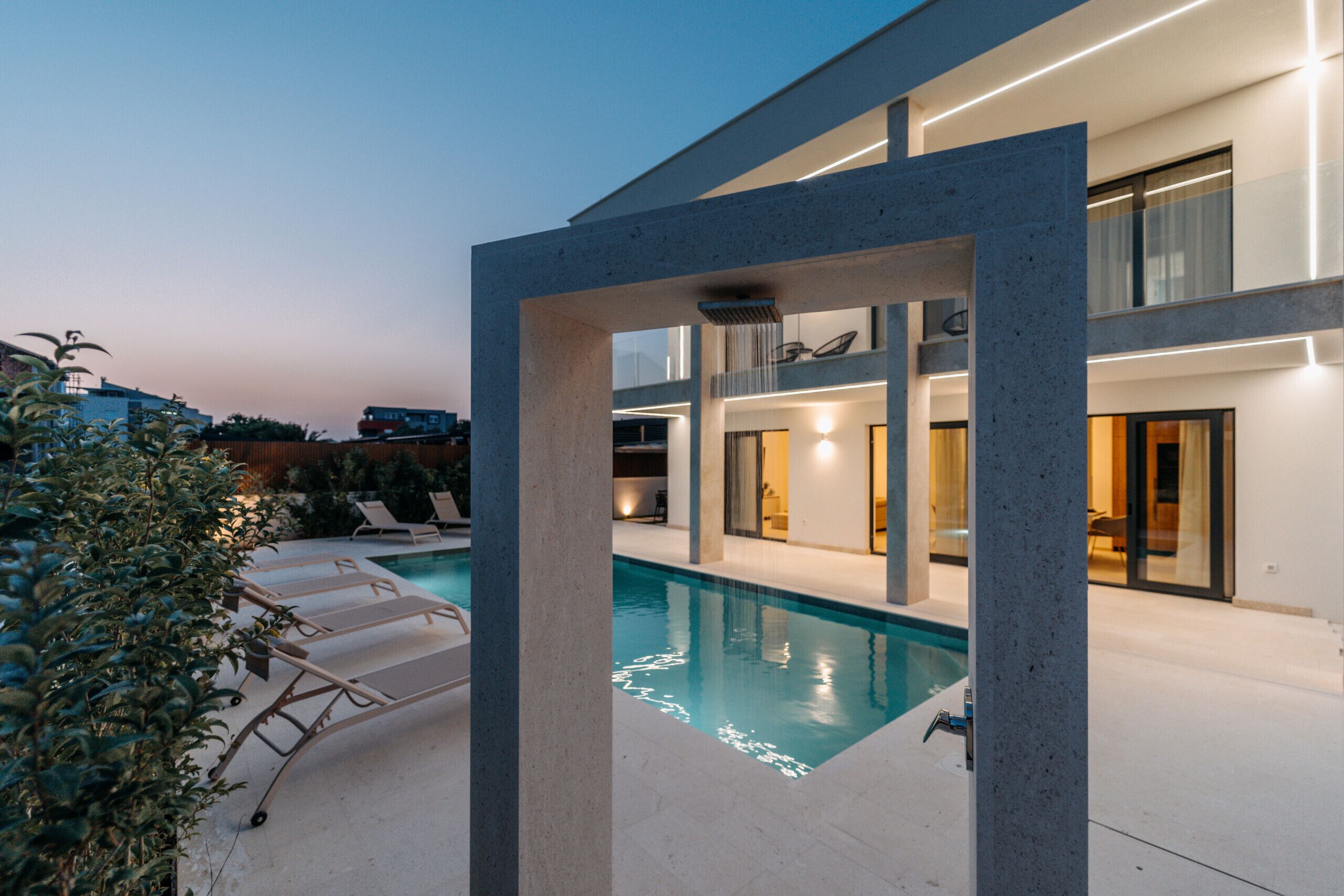 Une maison moderne dotée d’une piscine, de chaises longues et d’un intérieur bien éclairé.