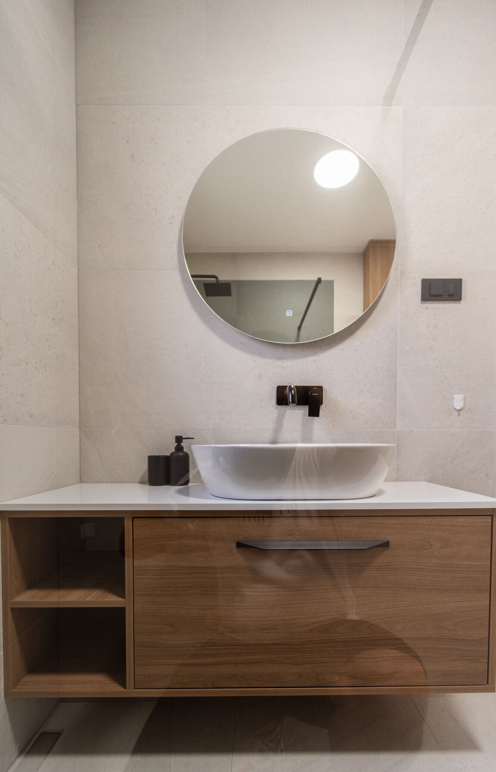 Une salle de bain moderne avec un lavabo blanc, un miroir rond et un meuble-lavabo en bois.