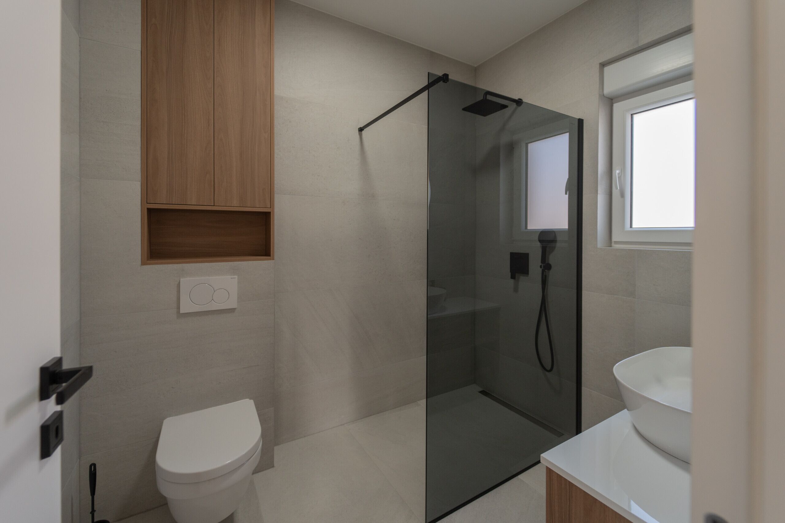 A modern bathroom with a glass-enclosed shower, a toilet, and a sink with a mirror above it.