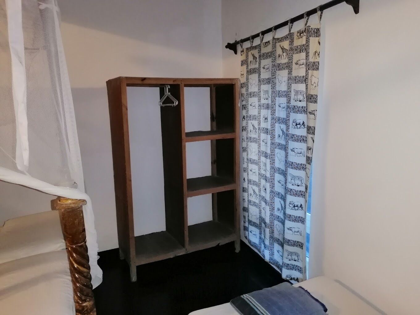 Una habitación de esquina con un armario de madera, un perchero y una cortina estampada.