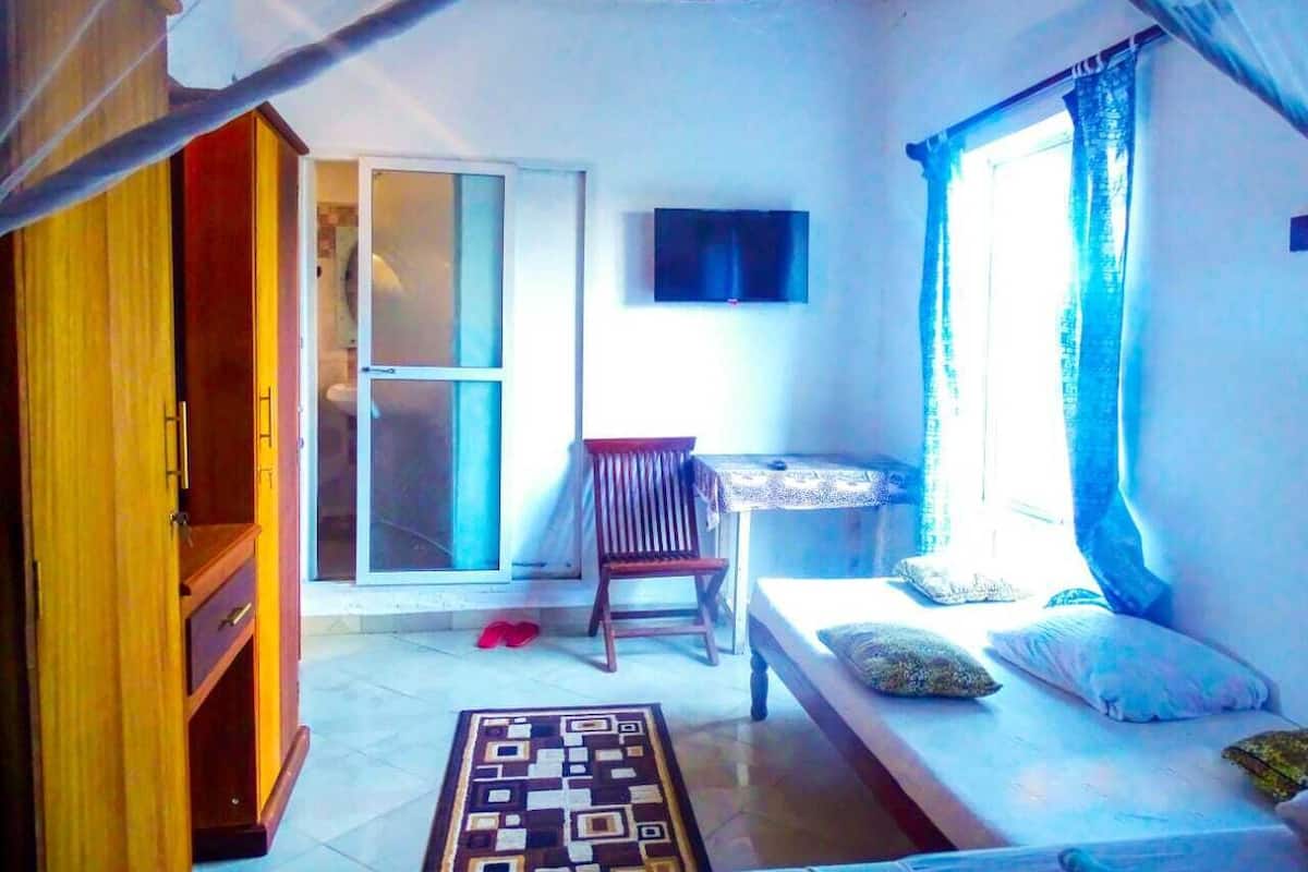 Une petite pièce comprenant un lit, une chaise, une petite table et un téléviseur.