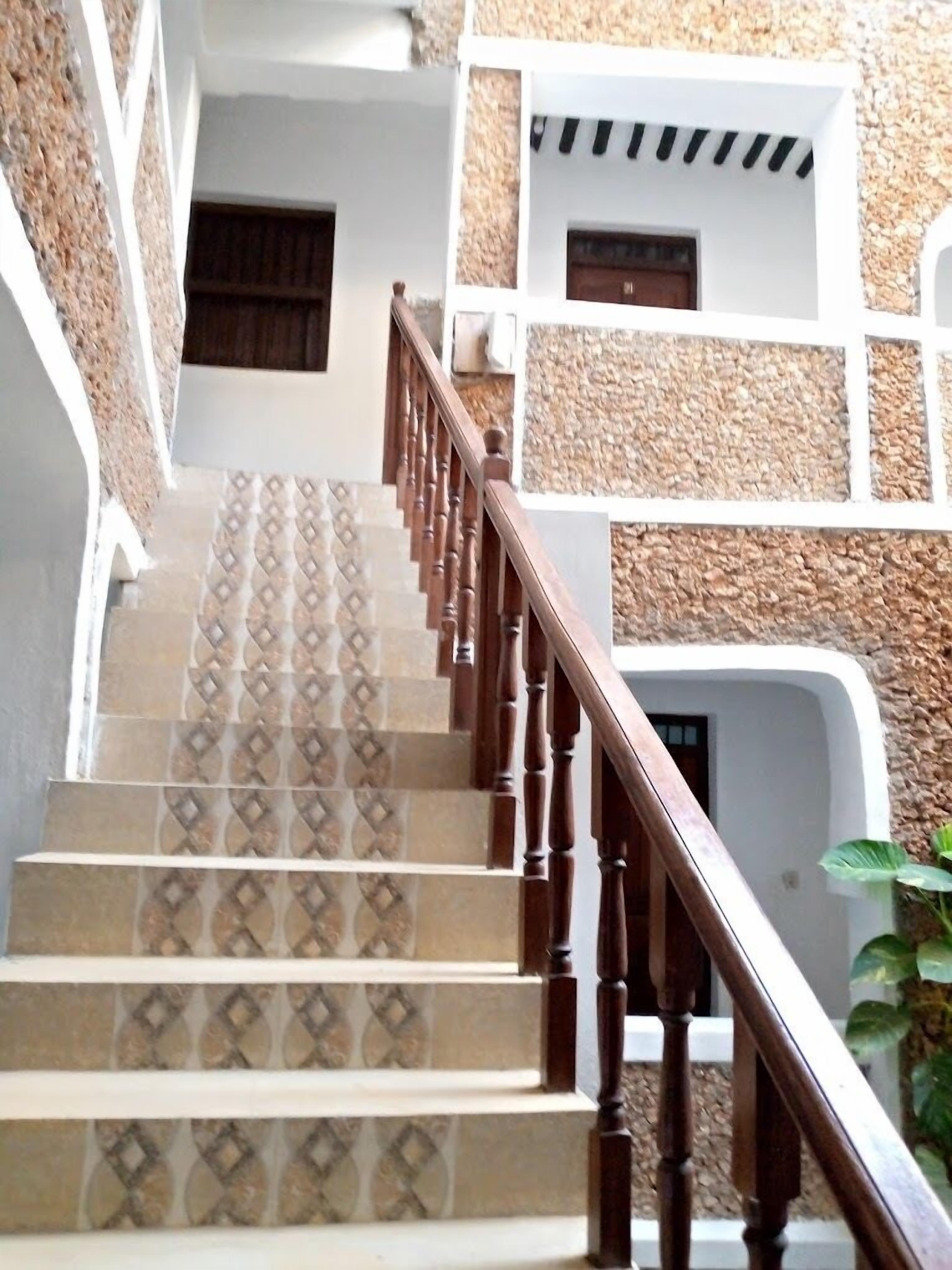 A staircase with patterned tiles and wooden railings leading to a building with white walls and stone accents.