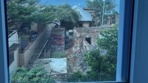 Vista pela janela de uma área costeira com edifícios, vegetação e um corpo de água.