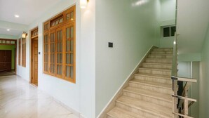 Un hall d’entrée spacieux avec un escalier, des portes en bois et un mur de couleur vert clair.