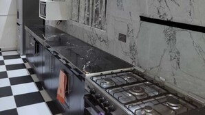 Een keuken met een zwart-wit geruite vloer, een gasfornuis, witte kasten en een marmeren spatwand.