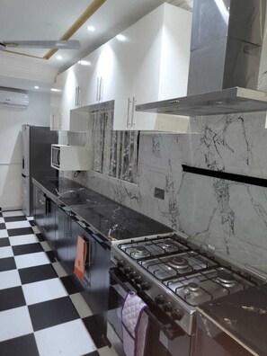 Una cocina con piso a cuadros blanco y negro, estufa a gas, gabinetes blancos y salpicadero de mármol.