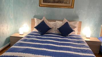 Una cama con colcha azul y blanca a rayas, dos almohadas y dos lámparas de noche.