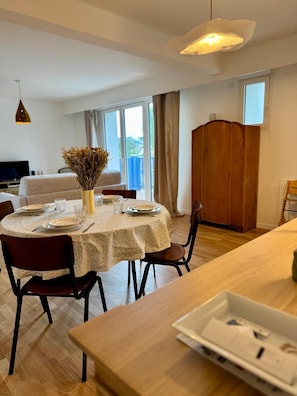 A dining area with a round table set for four, a vase with dried flowers, and a wooden cabinet in the background. - THE REPAIR NORMAND (Tourgéville)