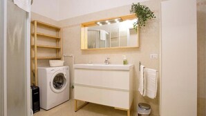 A compact bathroom with a washing machine, a sink, a mirror, and a small trash bin. - CASA AL GELSO, authentic Tuscan atmosphere (Lucca)