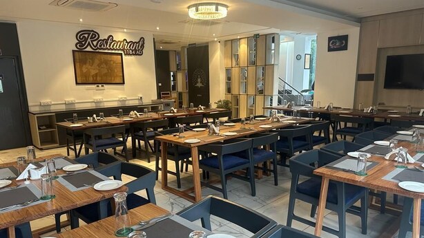 Un restaurant doté de plusieurs tables et chaises, d’un lustre et d’une enseigne fixée au mur.