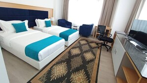 Une chambre d’hôtel avec deux lits, un bureau, une chaise, une télévision et une fenêtre avec des rideaux.