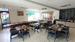 Un grand espace à manger avec plusieurs tables et chaises, un coin cuisine doté de placards et une grande fenêtre laissant entrer la lumière naturelle.