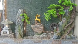 Un mur décoratif dans un jardin, agrémenté d’une sculpture de cerf, d’une lanterne et d’un tronc d’arbre rustique.