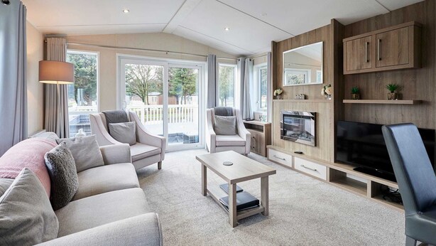Ein modernes Wohnzimmer mit einer Couch, Sesseln, einem Couchtisch und einem Fernseher. Ein Kamin, ein großes Fenster und ein Balkon mit Vorhängen sind ebenfalls vorhanden.