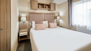 Ein Hotelzimmer mit einem großen Bett, einem Holzkopfende, Nachttischen, Lampen und eingebauten Regalen über dem Bett.