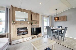 Ein modernes Wohnzimmer mit Fernseher, Holzschränken, einem Essbereich mit Stühlen und einem Kamin.