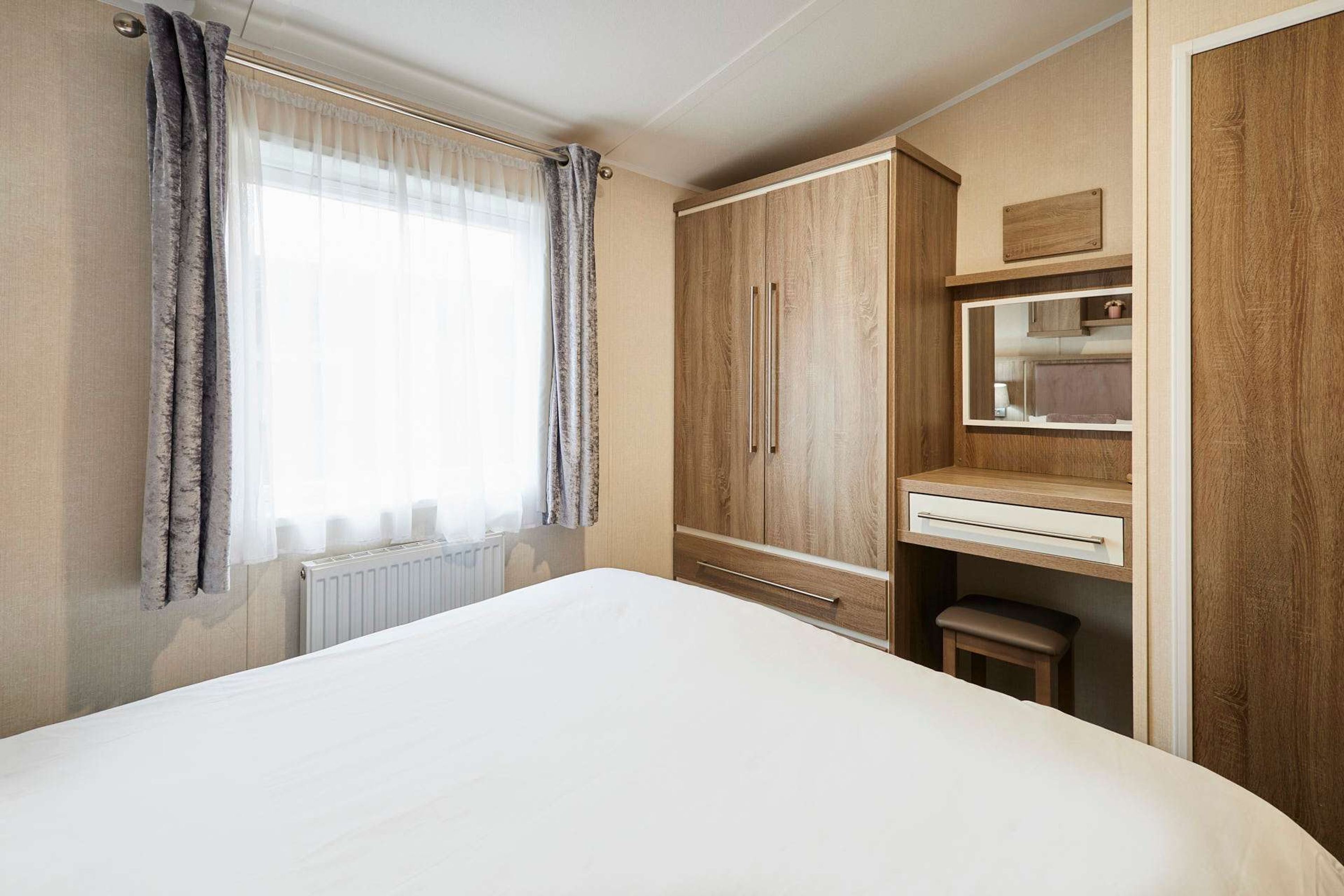 A bedroom with a large bed, wooden wardrobe, and a small desk with a mirror.