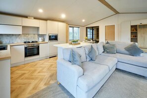 A modern kitchen with built-in appliances, a herringbone wood floor, and a grey sofa with cushions. - Host Stay Mulberry Lodge (York)