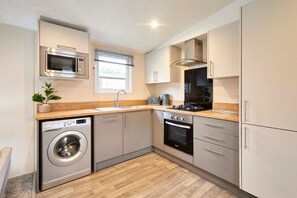 A compact kitchen with a washing machine, microwave, oven, and a sink. - Host Stay Dakota Lodge (York)