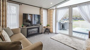 Una sala de estar moderna con una televisión de pantalla plana, un sofá, una pequeña mesa con plantas y un gran ventanal corredizo que da a un área exterior con un jacuzzi.