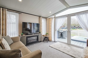 Ein modernes Wohnzimmer mit Flachbildfernseher, einer Couch, einem kleinen Tisch mit Pflanzen und einer Schiebetür zu einem Außenbereich mit Whirlpool.