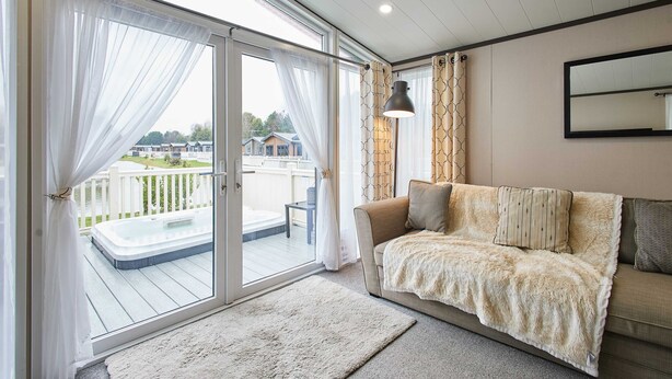 Una sala de estar acogedora con sofá, un ventanal con cortinas, un jacuzzi y vistas a una terraza y algunas casas.