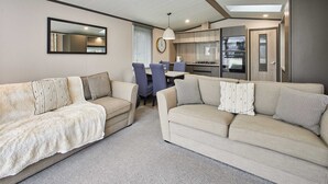 Una sala de estar moderna con dos sofás color beige, una mesa de comedor y una zona de cocina con electrodomésticos integrados.