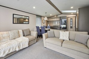 Ein modernes Wohnzimmer mit zwei beigen Sofas, einem Esstisch und einer Küchenzeile mit integrierten Geräten.