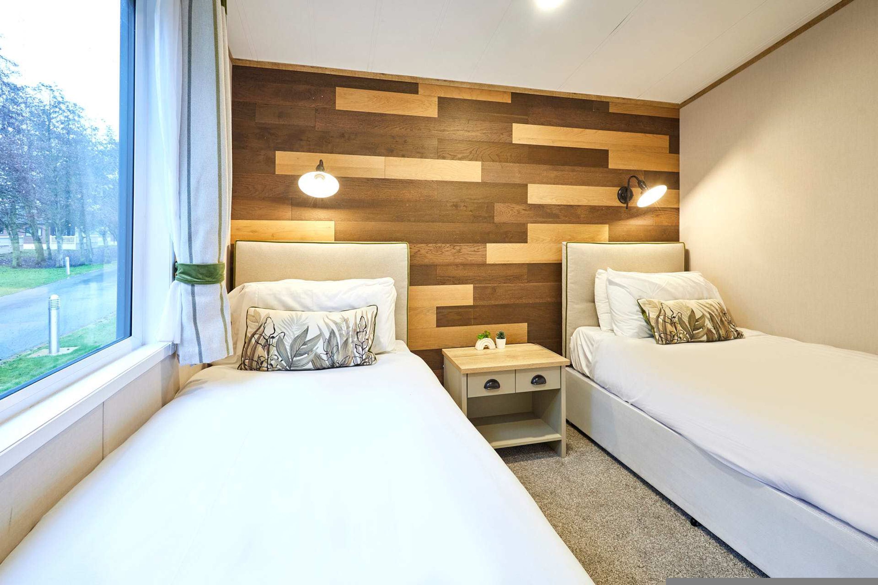 A hotel room with two beds, a wooden accent wall, bedside lamps, and a view of the outdoors.