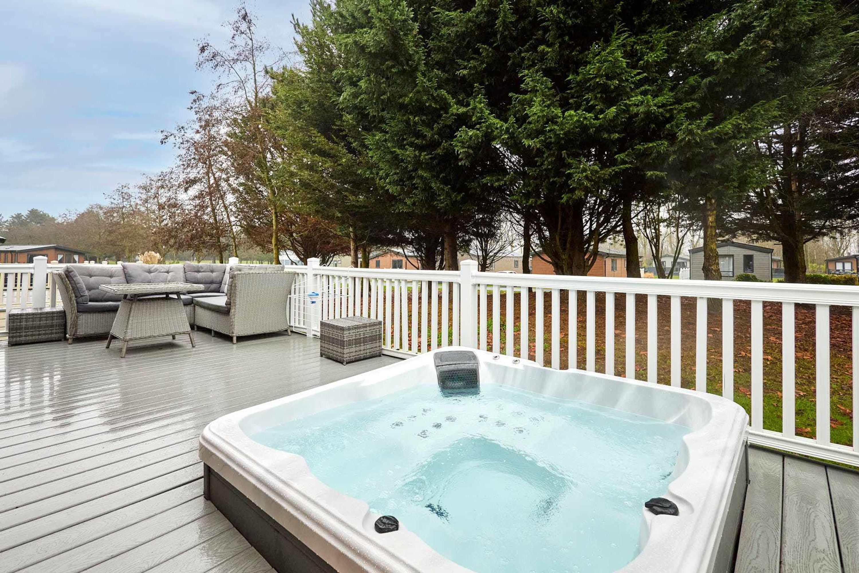 Ein Whirlpool auf einer Holzterrasse mit Gartenmöbeln und einem weißen Zaun.