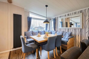 A modern dining area with a wooden table, grey upholstered chairs, and a pendant light. - Host Stay Four Seasons Lodge (York)