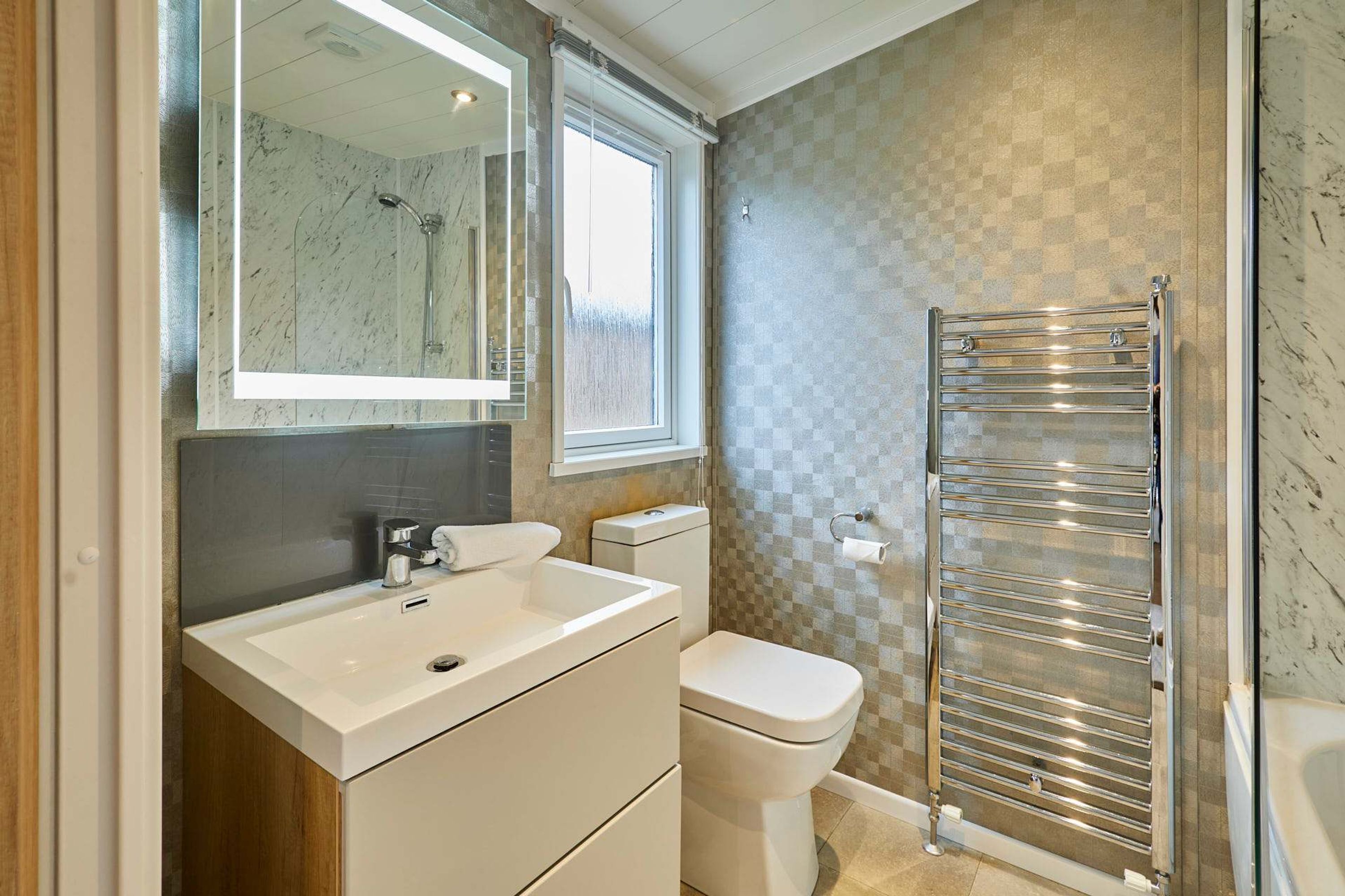 Une salle de bain moderne avec un lavabo blanc, des toilettes, une douche avec une porte en verre et un porte-serviettes.