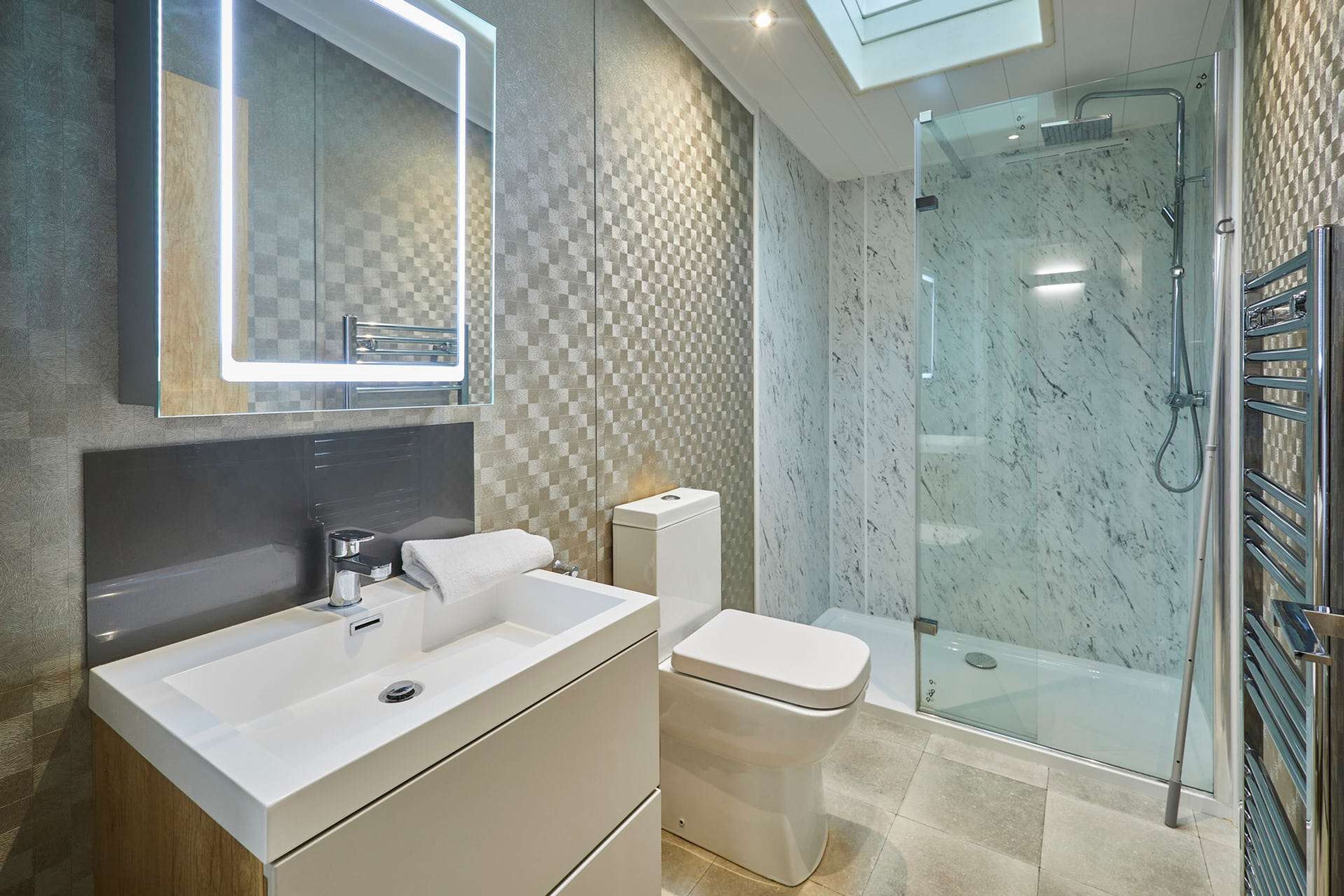 A modern bathroom with a large mirror, a sink, a toilet, and a glass-enclosed shower area.