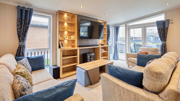 A modern living room with a large flat-screen TV, built-in shelves, a wooden coffee table, and a sofa with patterned cushions. - Host Stay Four Seasons Lodge (York)