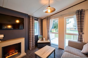 A cozy living room with a fireplace, a sofa, a table, and a TV mounted on the wall. - Host Stay Oakwood Lodge (York)