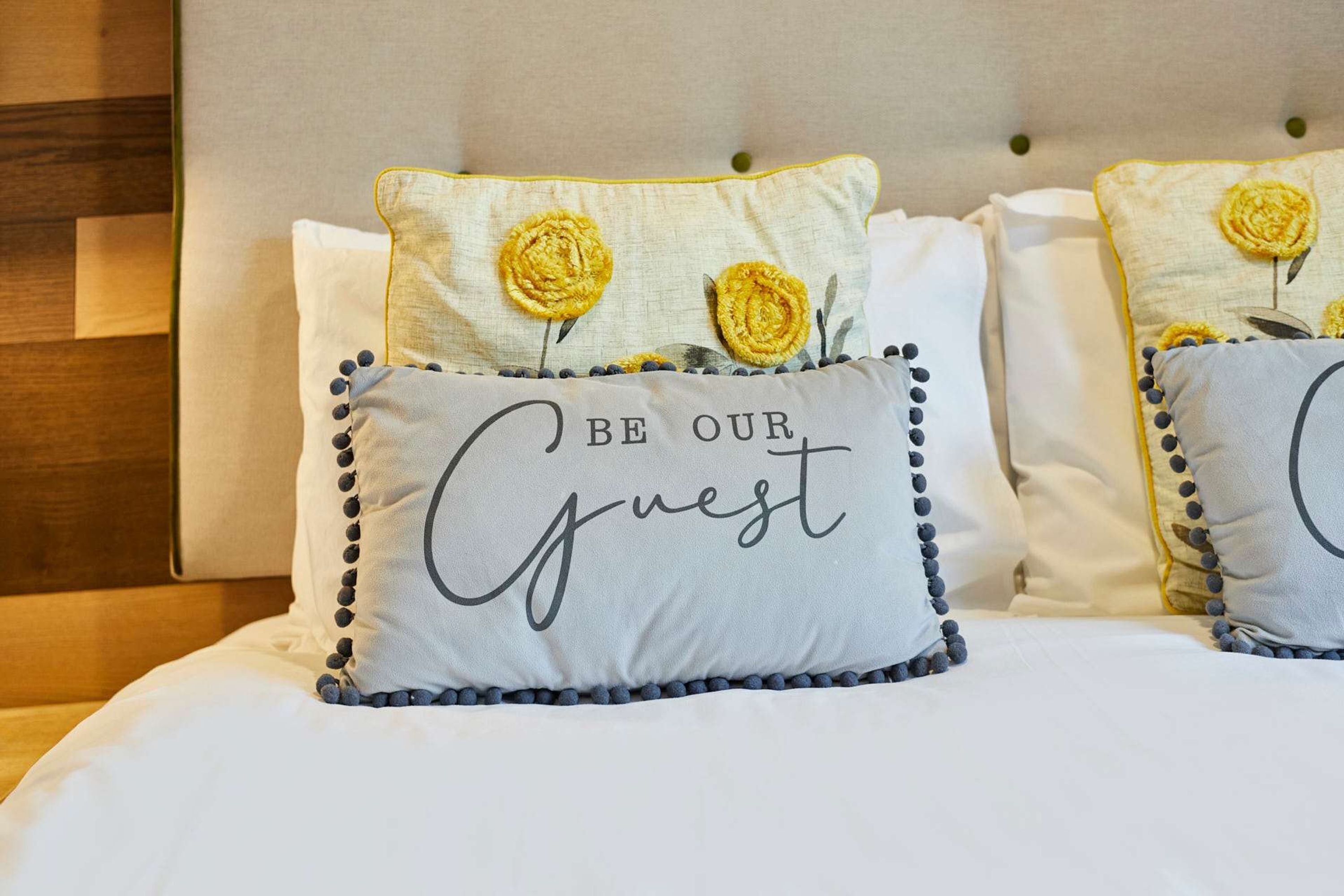 A bed with pillows featuring embroidered text and decorative flowers.