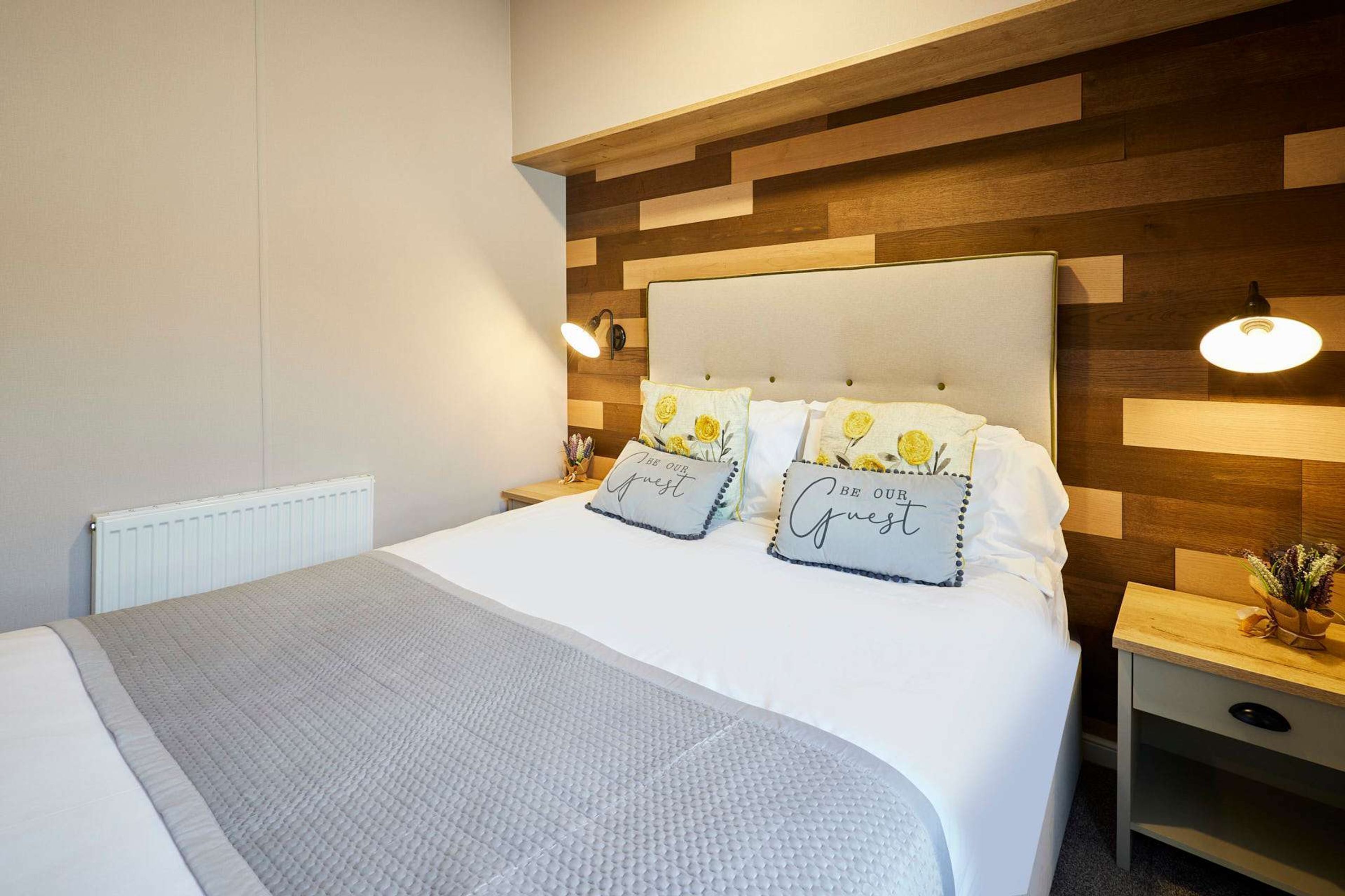A neatly made bed with a grey quilt, two pillows with floral designs, and a wooden headboard.